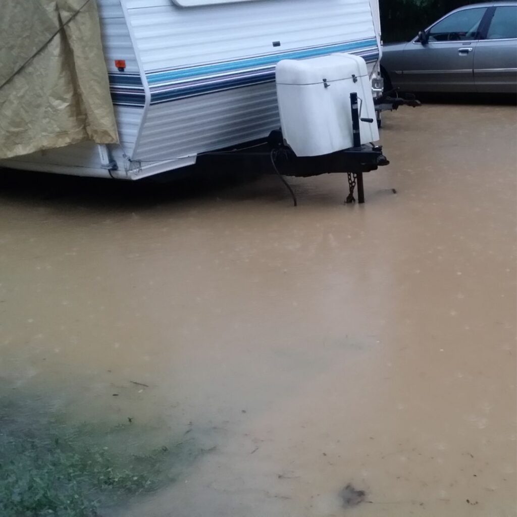 a flooded driveway with a recreational vehicle and a car parked on it